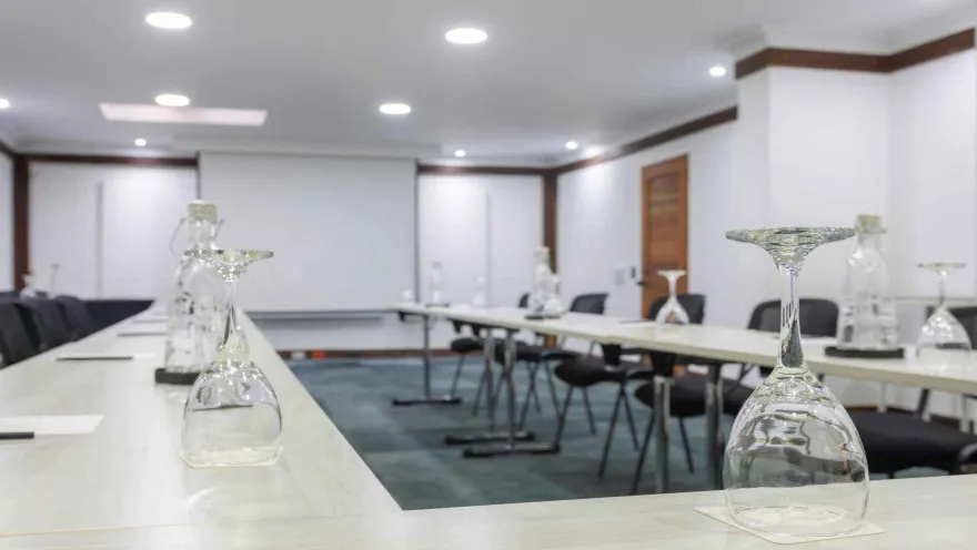Sala de conferencias preparada con mesas largas y copas invertidas. 