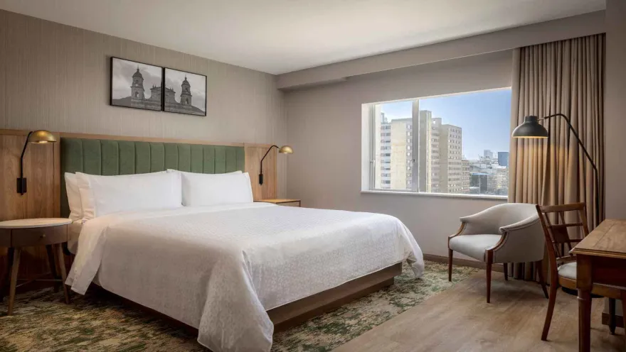 Habitación de hotel con cama king-size, cabecera verde y vista a la ciudad.