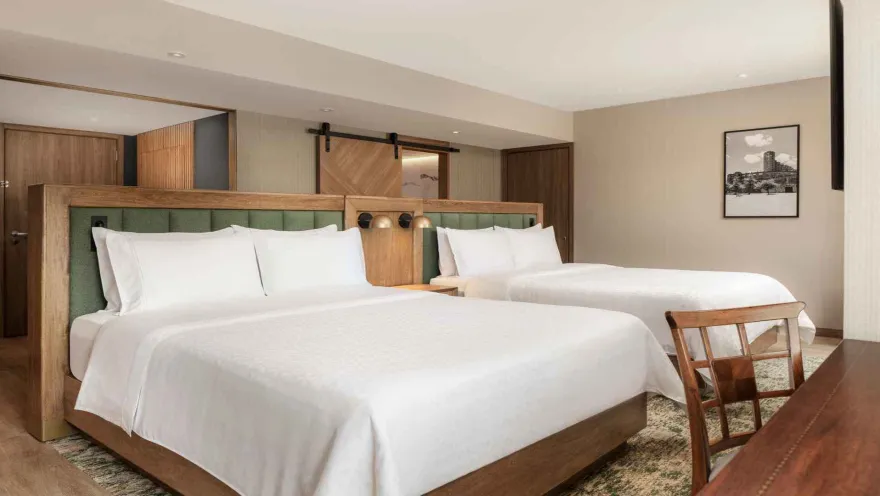 Habitación de hotel con dos camas dobles, cabeceras verdes y puerta corrediza.