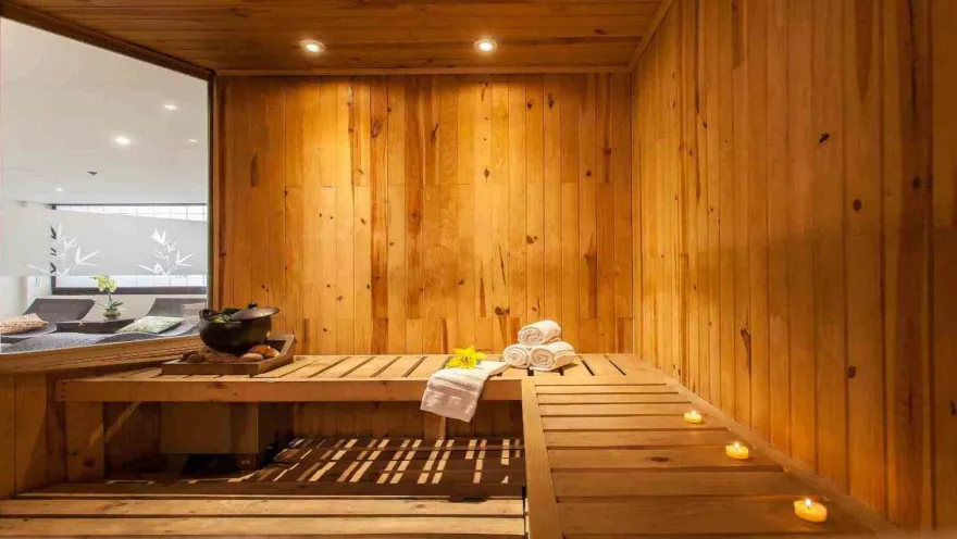 Una sauna de madera cálida y acogedora, con toallas apiladas y velas que añaden un toque de tranquilidad.