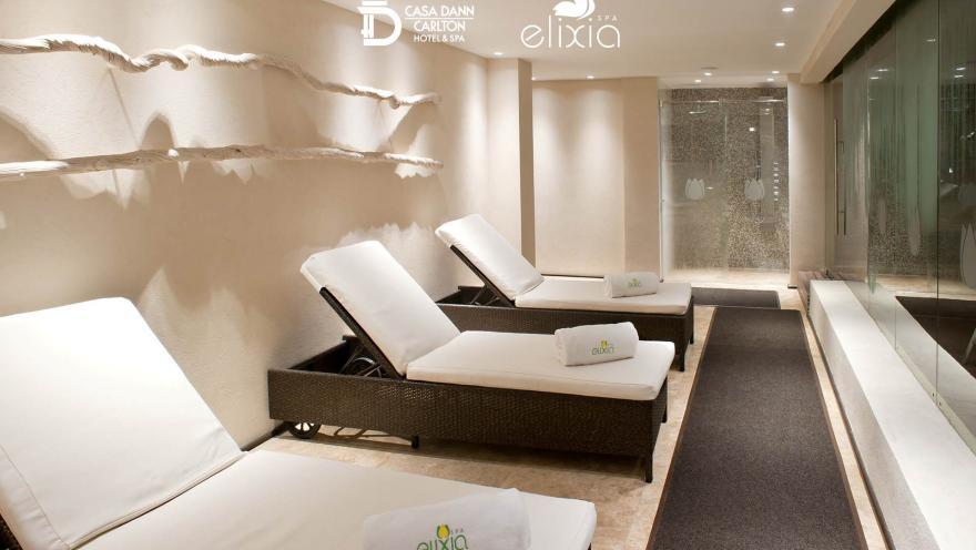  Salón estilo sauna o turco cuyas paredes son de cristal y concreto. Hay tres sillas amplias, cada una con toallas, dispuestas para que las personas se recuesten en ellas.