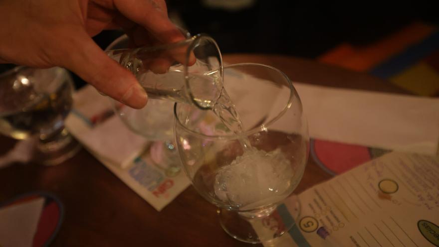 Una mano en primer plano sirve de una copa a otra algo que parece ser licor.