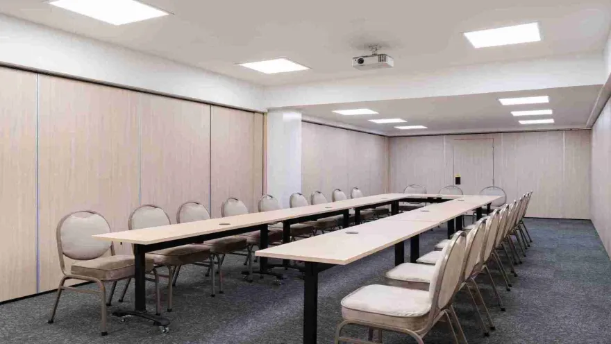Una sala de reuniones dispuesta en forma de "U" con mesas y sillas cómodas, equipada con un proyector, ideal para conferencias y presentaciones.