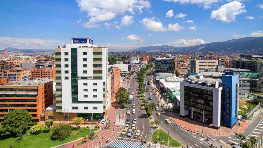 Una vista aérea de una bulliciosa calle de la ciudad con edificios modernos y montañas al fondo. El "Hotel Andes Plaza" se destaca en el paisaje urbano.