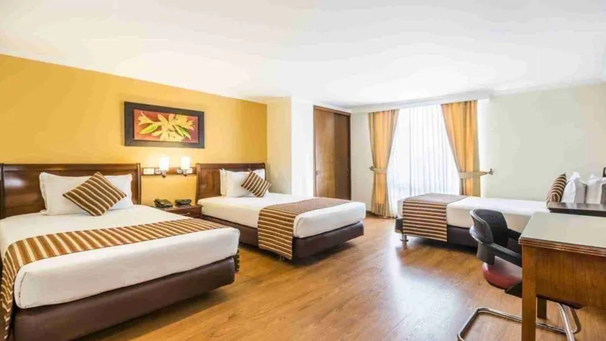 Un dormitorio triple de hotel con tres camas individuales, ideal para grupos o familias. La habitación cuenta con escritorio y un diseño funcional en tonos cálidos.
