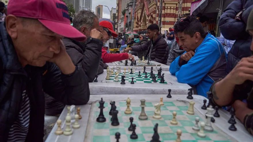 Men play chess at several tables set up on a street.