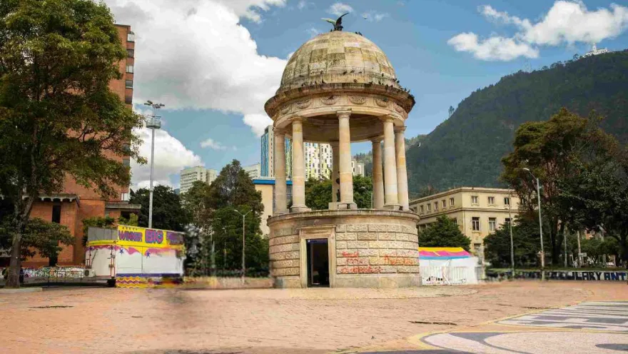 Stone pavilion seen from below. A decorative bird figure stands out atop its dome. Several trees surround it.