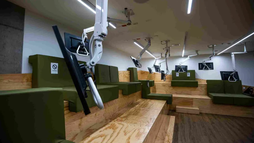 A room featuring several television screens suspended from the ceiling and positioned in front of comfortable sofas.
