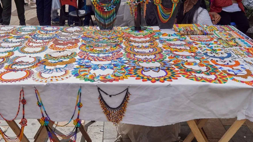 A collection of handcrafted necklaces in the colors of the Colombian flag are displayed on a table.