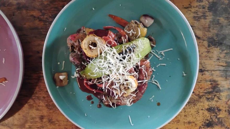  Vista cenital de un plato turquesa con una comida que consiste en carne cocinada, verduras asadas y una pizca de queso rallado.