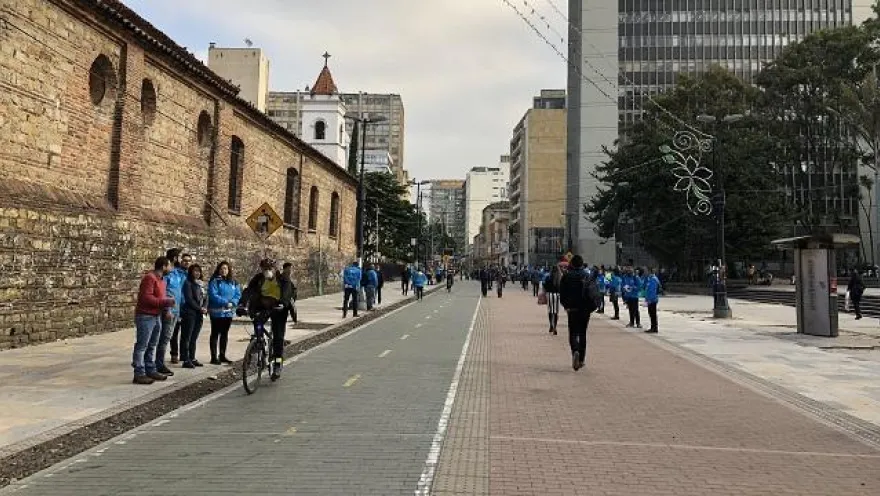 En el centro, la Carrera Séptima luce organizada y abierta, con un carril para bicicletas y amplios espacios para peatones. Personas caminando, conversando y un ciclista en movimiento reflejan un ambiente tranquilo y dinámico, enmarcado por edificios modernos y árboles que aportan equilibrio al paisaje urbano.