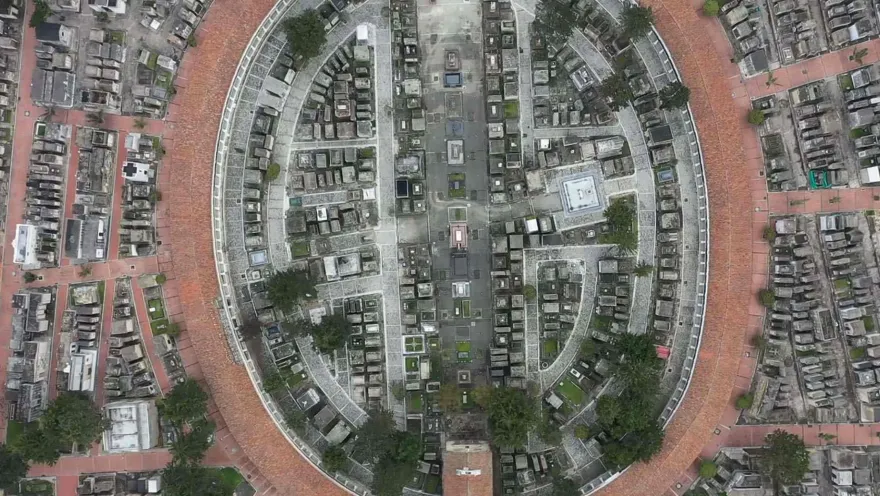 Aerial view from a drone showing a circular panorama of the central cemetery. Brick pathways, laid out in a labyrinthine style, and some trees are prominent features.