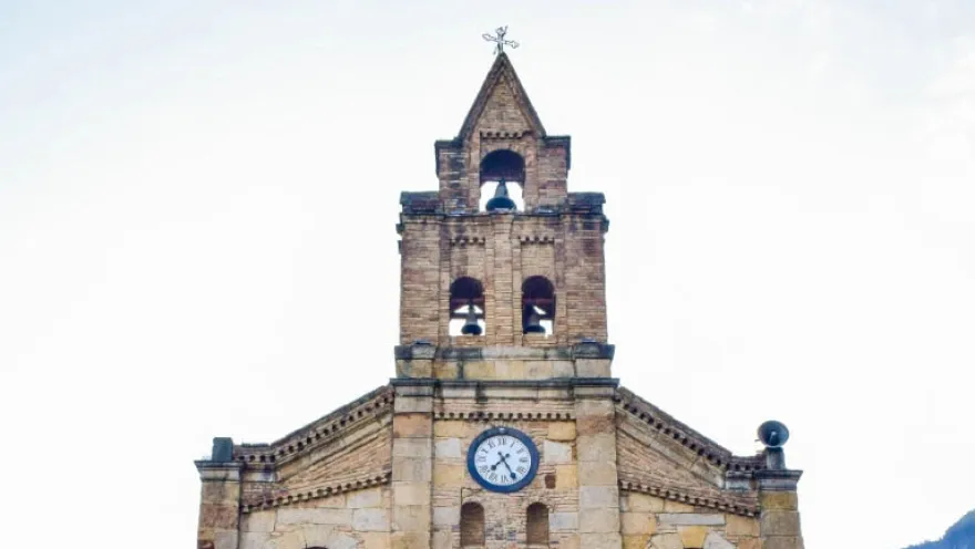 Close-up of the upper part of the stone church, highlighting the tower with its bell tower and clock.