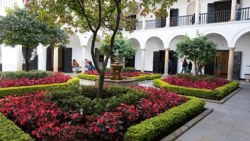 The Botero Museum's interior garden, completely adorned with red and green flowers on the ground. There's a fountain in the center.