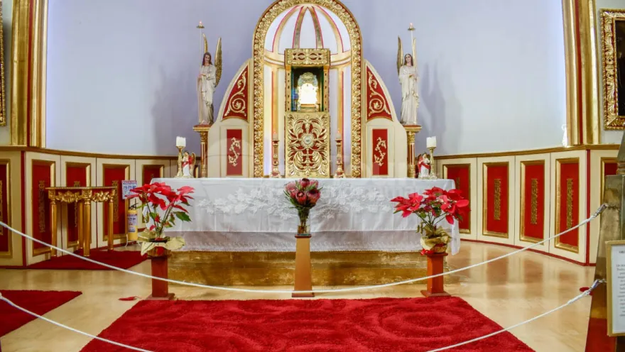 Close-up of the parish church's interior, showing the altar decorated with three floral arrangements and several red rugs.