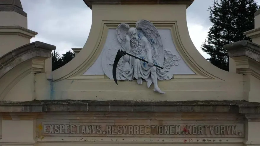 Close-up of a figure that appears to be Death, holding a black scythe, atop a facade.