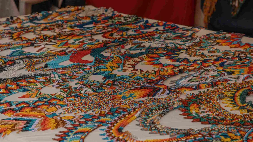 Close-up of a table displaying various handicrafts, such as necklaces and earrings, in the colors of the Colombian flag: yellow, blue, and red.