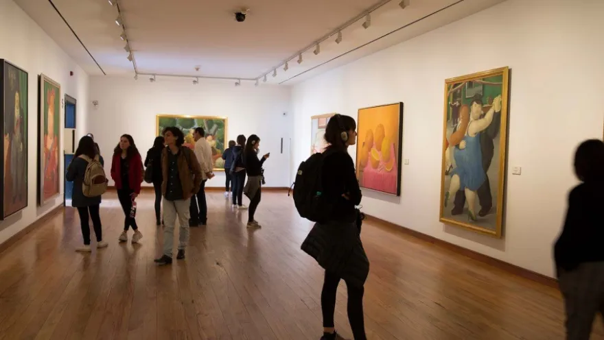 The interior of the Botero Museum's exhibition hall, where several young people are viewing paintings.