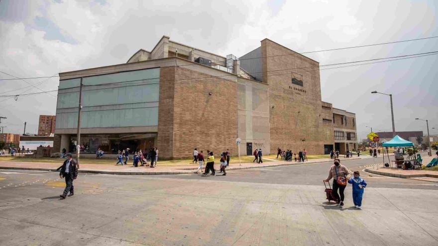 Exterior view of a modern brick and glass cultural building identified as ""El Ensueño"" (The Dream). Several people walk along the sidewalk and cross the street in front of the building, in an urban setting with cloudy skies.