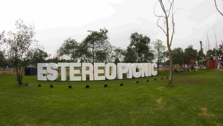 Letras gigantes blancas que forman “ESTÉREO PICNIC” en un parque verde, rodeadas de árboles y estructuras de festival al fondo.