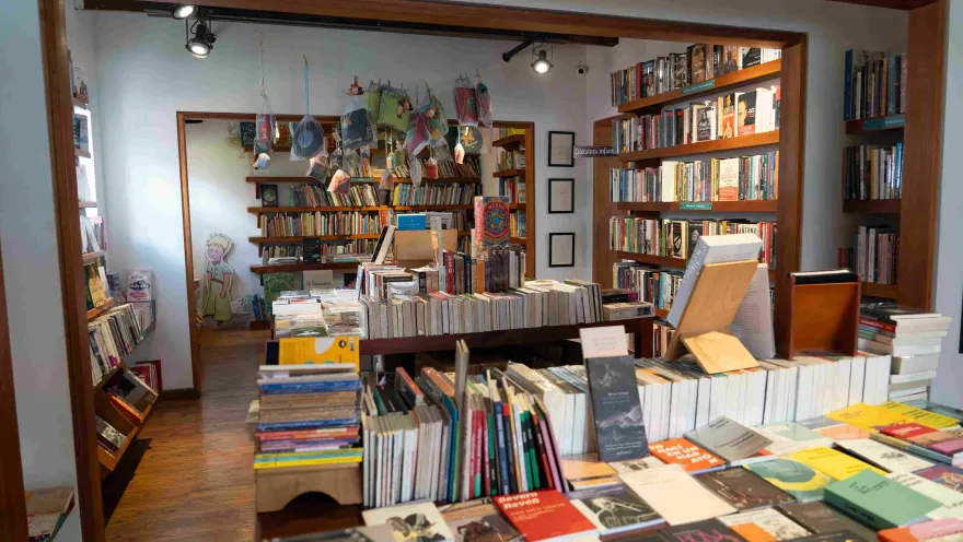 Interior de una librería con estanterías de madera llenas de libros, mesas de exhibición y una sección infantil al fondo decorada con ilustraciones.