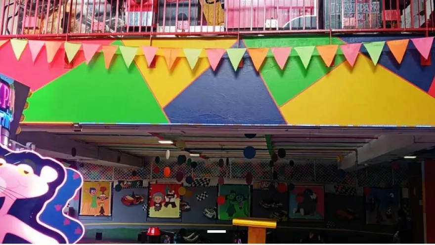 Fachada colorida de una zona de juegos interior con banderines, ilustraciones y letreros luminosos.
