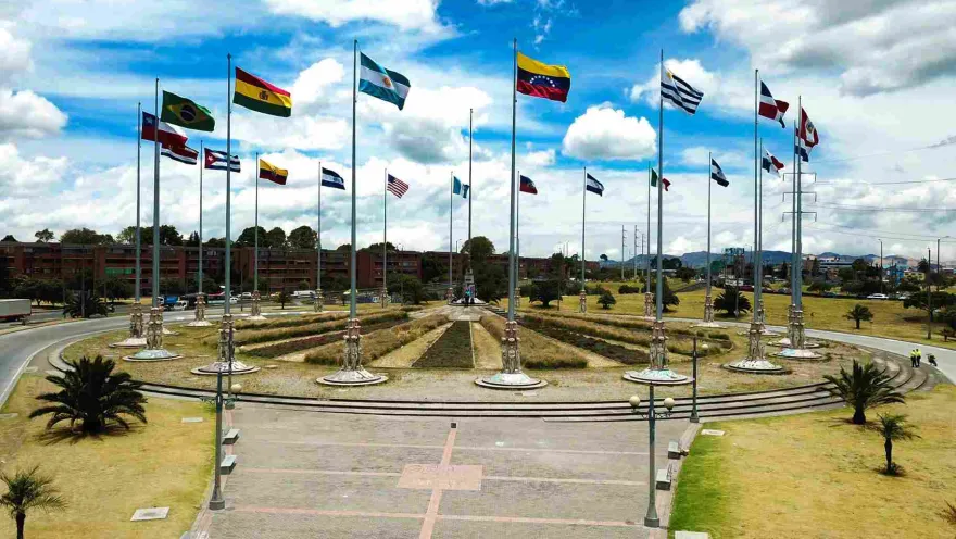  Monumento con múltiples banderas ondeando en una plaza abierta bajo cielo parcialmente nublado.
