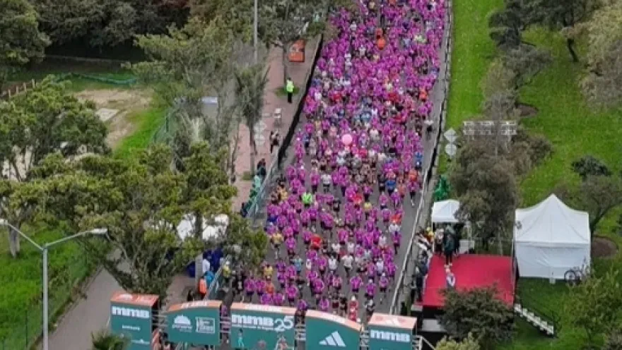 Vista aérea de una multitud de corredores vestidos de rosa avanzando por una vía durante una carrera.
