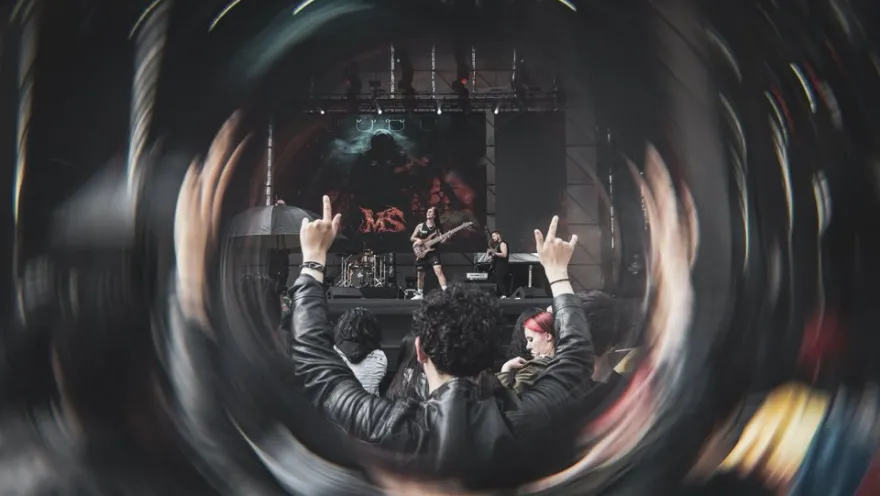 A rock concert audience raising their hands in front of the stage, seen through a circular effect that highlights the energy of the moment.