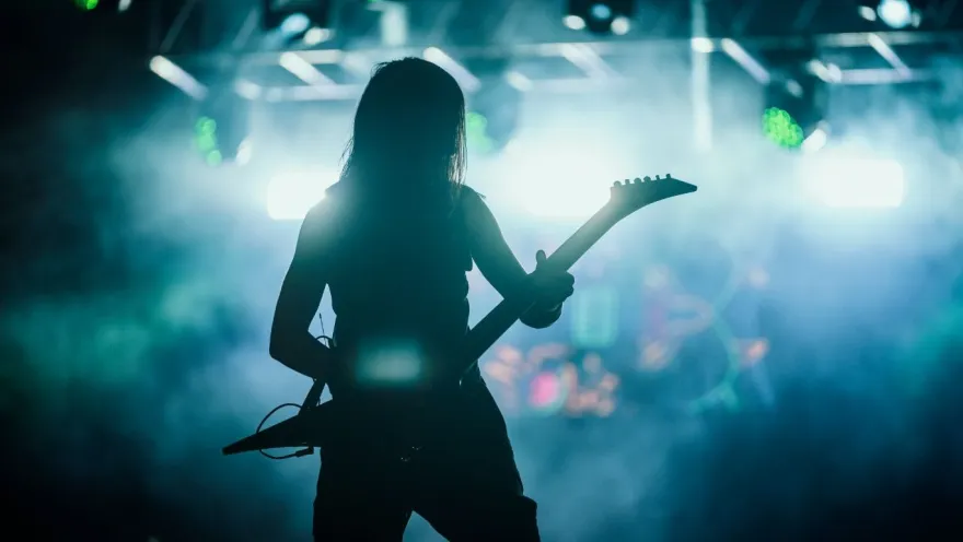 Silhouette of a guitarist in concert, illuminated by bright lights and smoke on stage during a live performance.