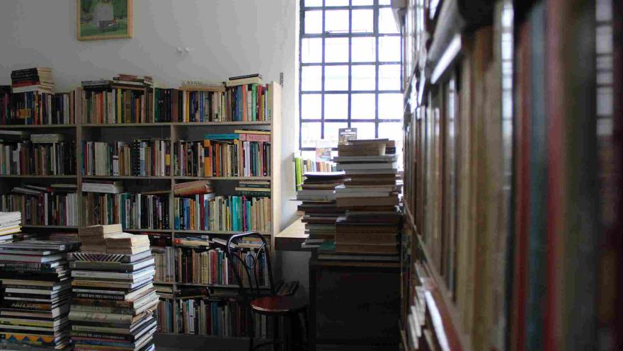 Interior of the bookstore with full shelves and stacks of books by a window.