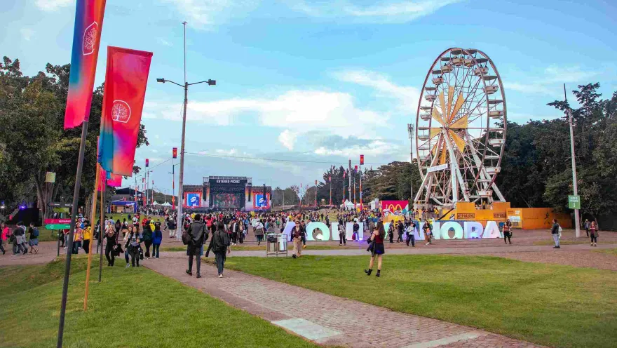A crowd at the Estéreo Picnic festival walking between stages, with a Ferris wheel and colorful flags in the background.