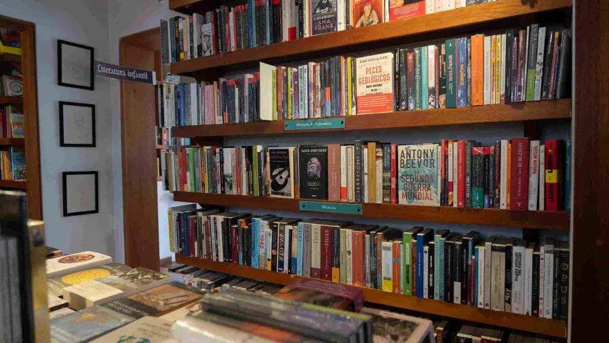  Estantería de madera llena de libros organizados por categorías, con títulos de historia y literatura en una librería.