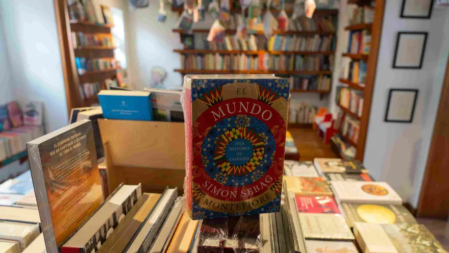 Libro “El mundo” de Simon Sebag Montefiore en primer plano sobre una mesa, con estanterías de libros desenfocadas al fondo en una librería.