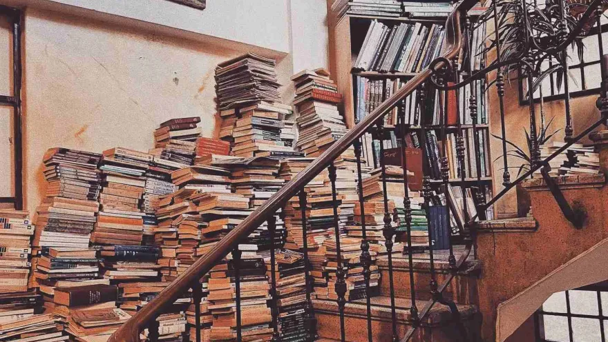 Interior staircase surrounded by shelves and numerous stacks of books, in a warm and inviting bookstore setting.