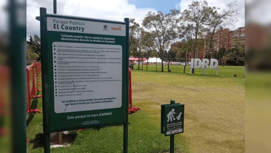 Aviso informativo del Parque Público El Country en primer plano, con amplias zonas verdes, árboles y el logo del IDRD visibles al fondo.