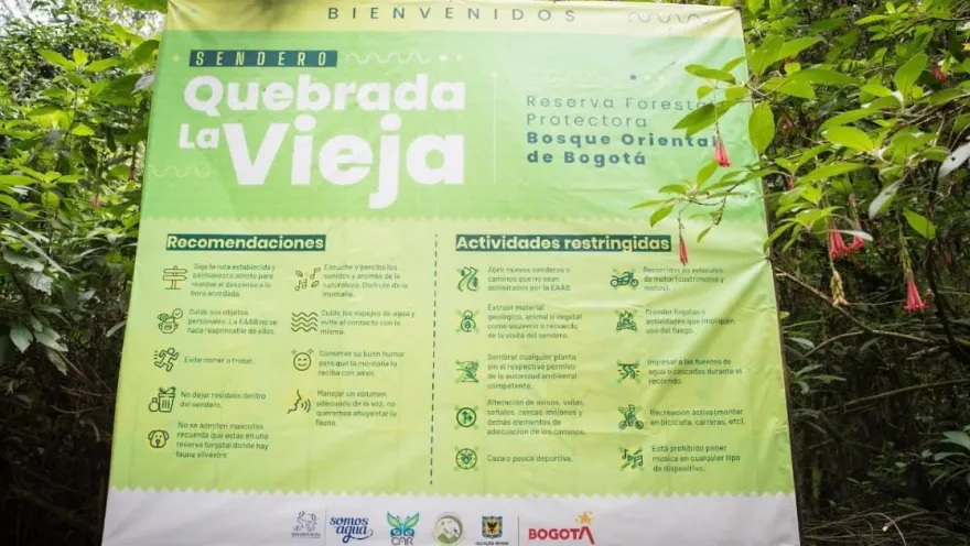 Aviso informativo del sendero Quebrada La Vieja, ubicado en la Reserva Forestal Protectora Bosque Oriental de Bogotá. El letrero, rodeado de vegetación, presenta recomendaciones para los visitantes y normas de conservación para proteger este entorno natural.
