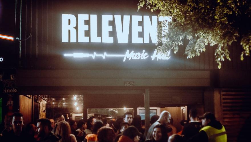 The illuminated facade of Relevent Music Hall at night, with a group of people gathered at the entrance under the establishment's illuminated sign.