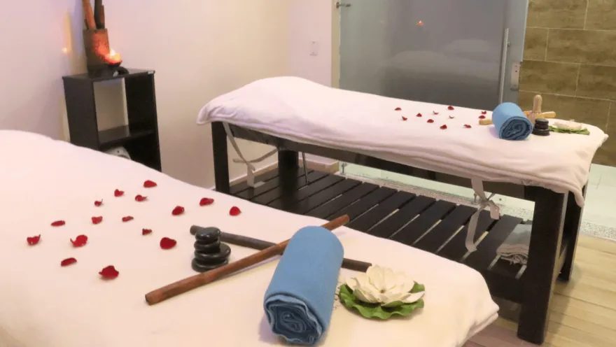 Sala de masajes con dos camillas decoradas con pétalos de rosa, toallas, piedras y elementos de relajación en un ambiente cálido y tranquilo.