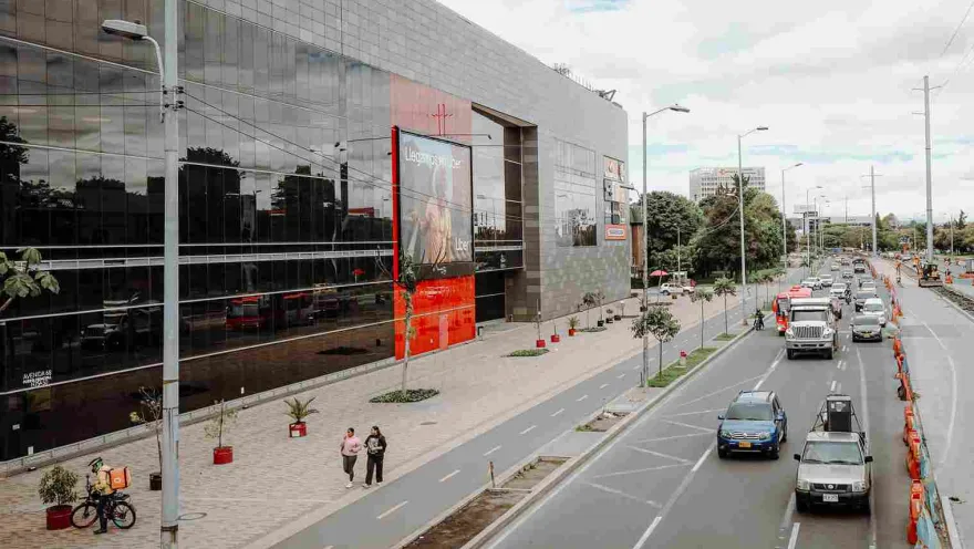 Una amplia avenida bordea la moderna fachada del Centro Comercial Metrópolis, donde el movimiento de vehículos, peatones y ciclistas refleja la dinámica cotidiana de este sector de Bogotá.