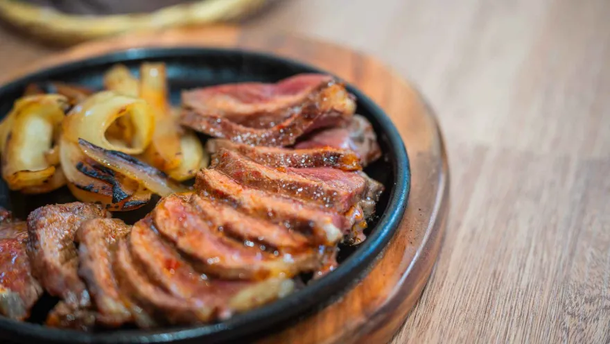 Medallones de carne de res jugosa tajados y servidos con cebollas asadas en un plato caliente de hierro.
