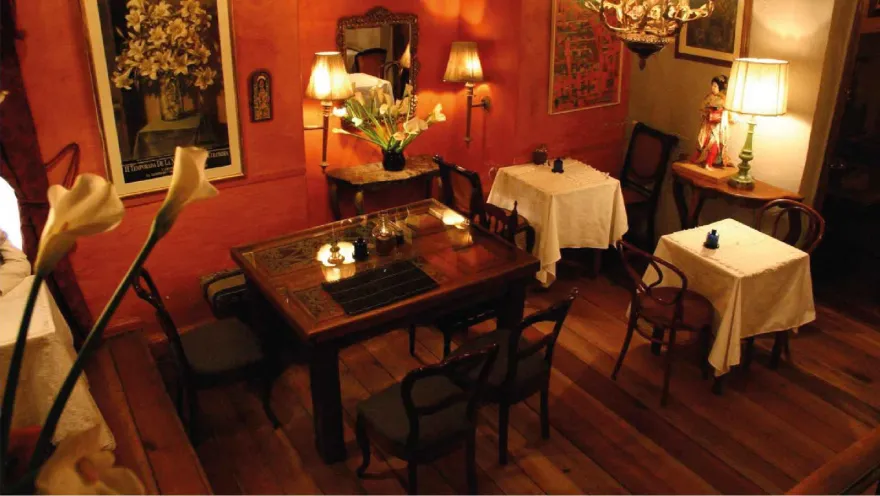 Vista superior de un salón con paredes rojas, suelo de madera, mesas vestidas e iluminación tenue de lámparas.