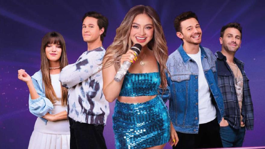 Cinco jóvenes sonrientes posando juntos; la chica del centro usa vestido azul deslumbrante y sostiene un micrófono.