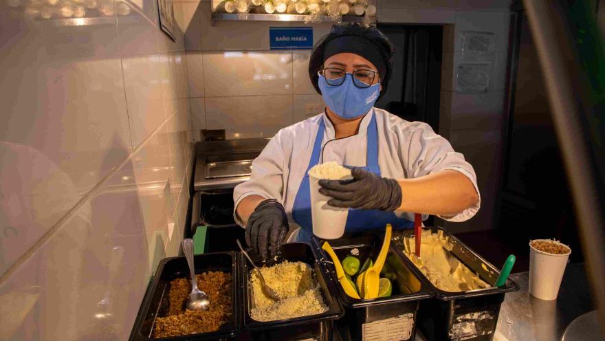 Cook preparing esquites with corn and various ingredients at the service station.