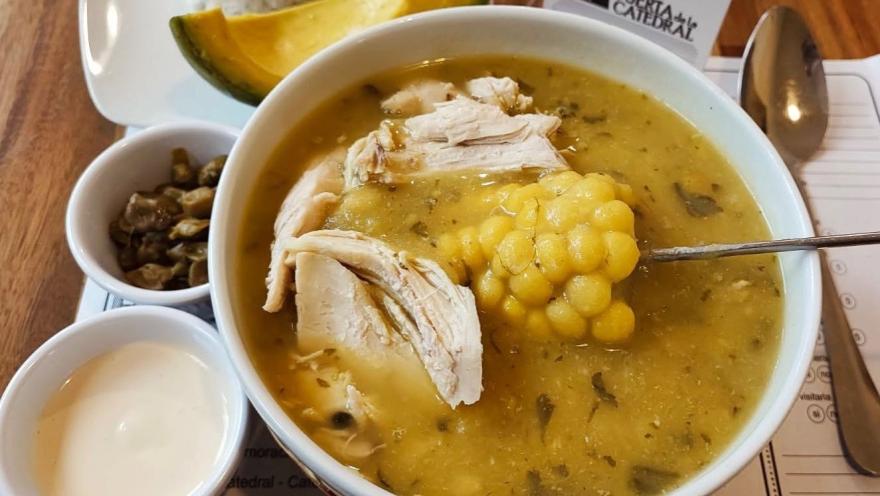 Ajiaco santafereño served with chicken, corn on the cob, and potato, accompanied by avocado and capers.