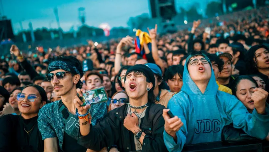 Multitud de jóvenes en un concierto al aire libre cantando y levantando las manos cerca del escenario.