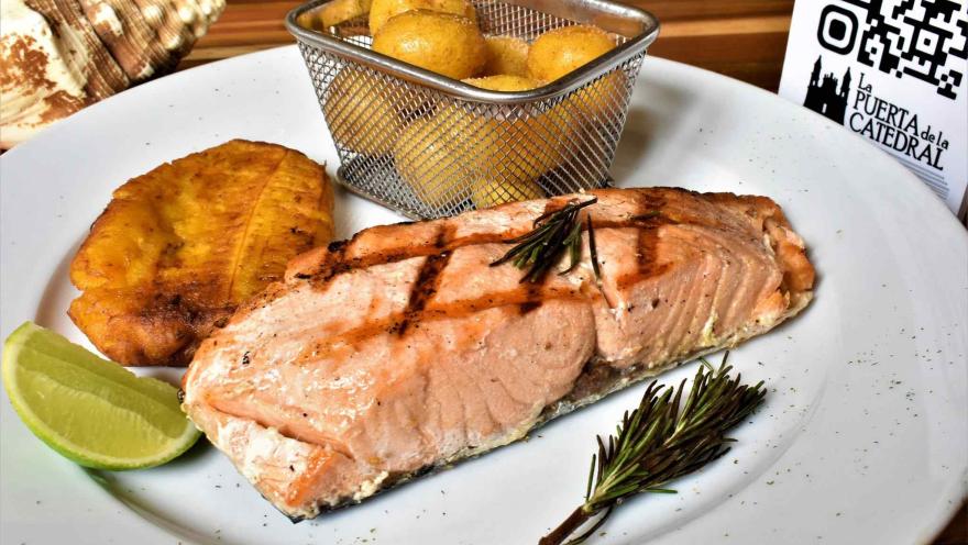 Grilled salmon fillet accompanied by a patacón, potatoes, and lemon. 
