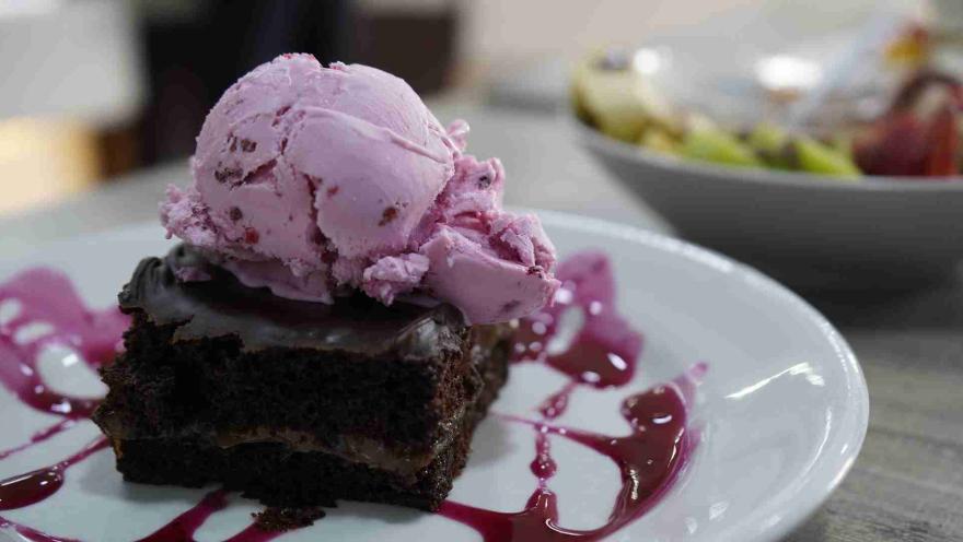 Una porción de brownie de chocolate con helado de fresa encima, decorado con salsa de frutos rojos en un plato blanco. 