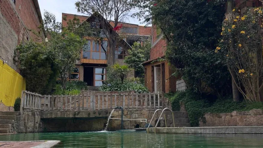 A pool surrounded by vegetation, stone walls, and brick-and-wood structures, with a small waterfall that creates a natural and peaceful atmosphere.