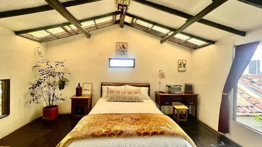  Habitación acogedora con cama doble, muebles de madera, techo con vigas expuestas y una ventana con vistas a los tejados.